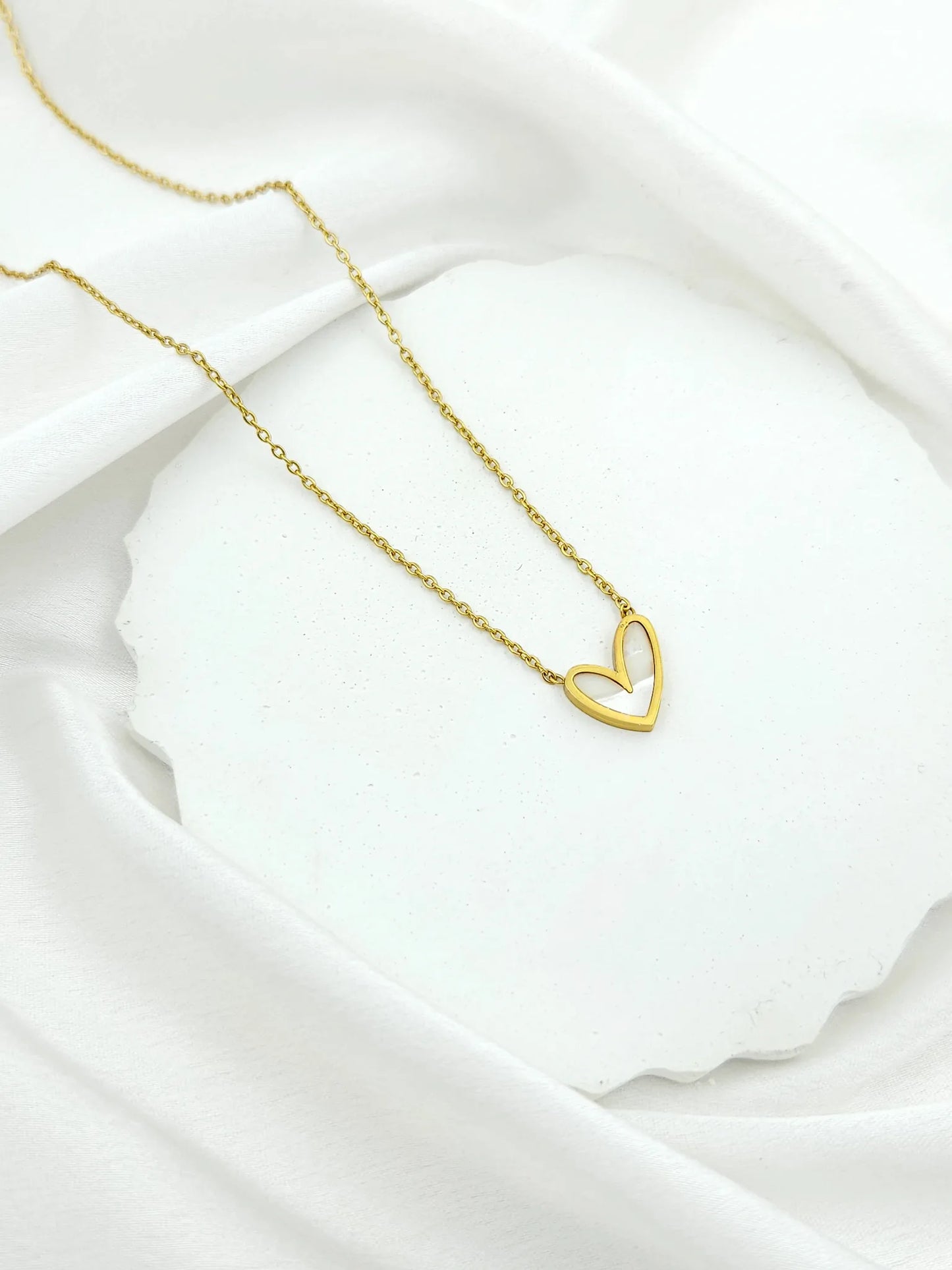 Gold heart-shaped necklace on a white fabric background