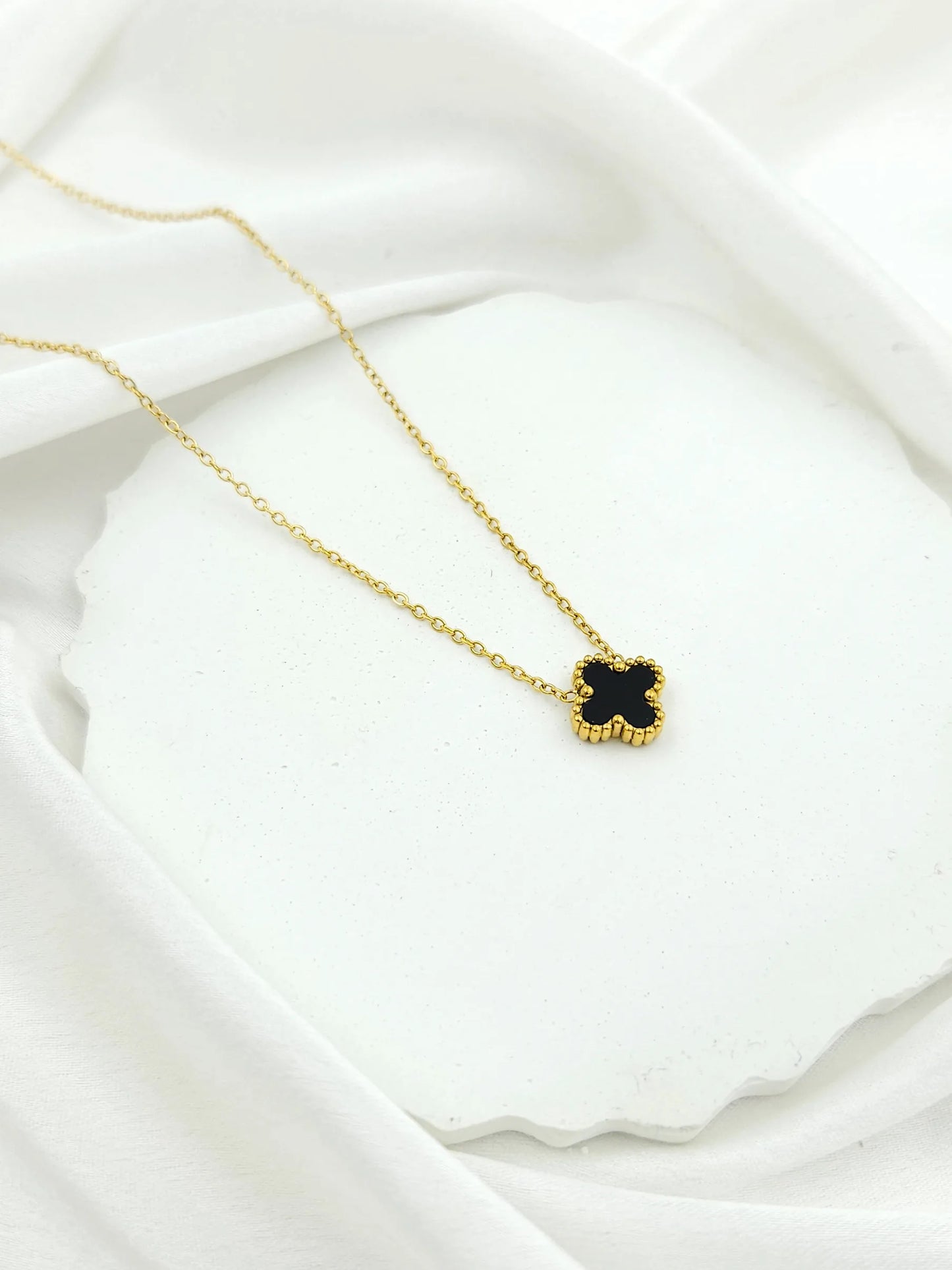 Gold necklace with a black pendant on a white fabric background