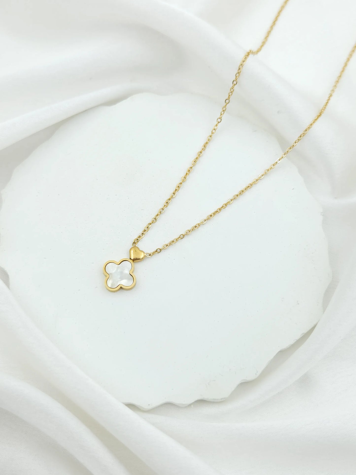 Gold necklace with a clover-shaped pendant on a white fabric background