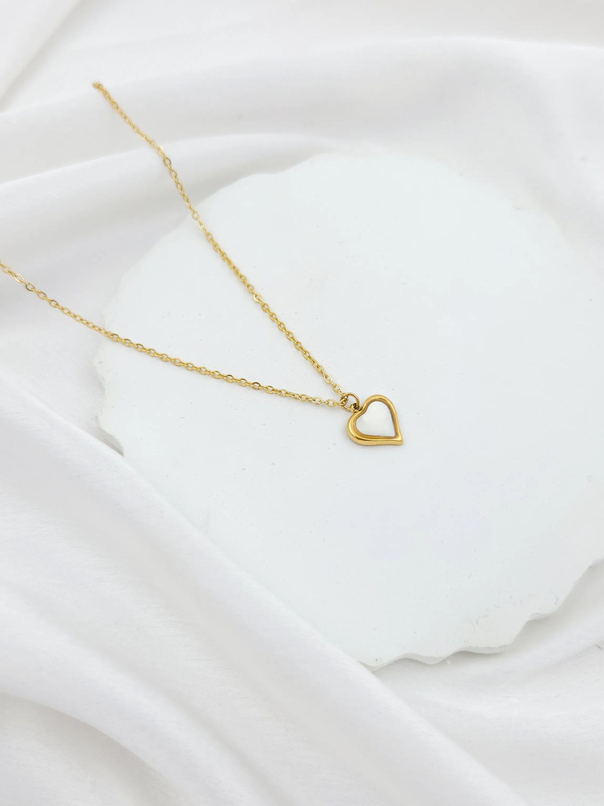 Gold necklace with a heart pendant on a white fabric background